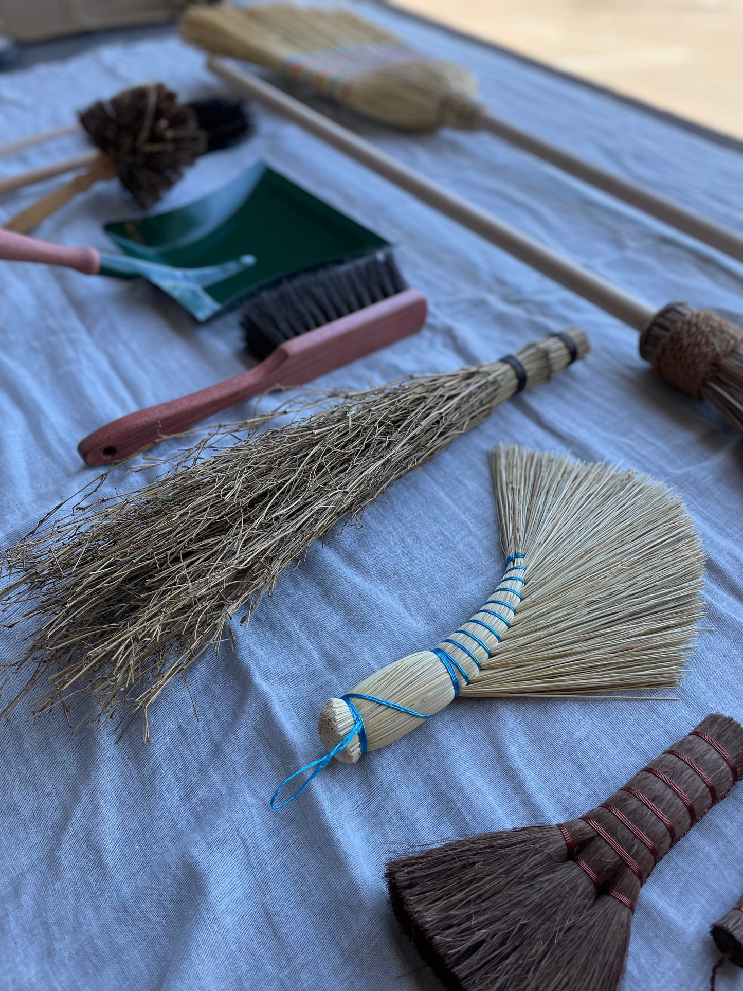 Display of various Redecker hand brushes and long handle brooms on cloth background