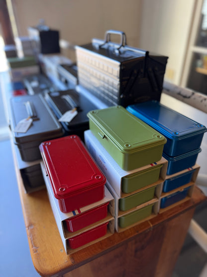 A collection of colorful metal tool boxes stacked on a wooden table, including red, green, blue, and black boxes in various sizes.