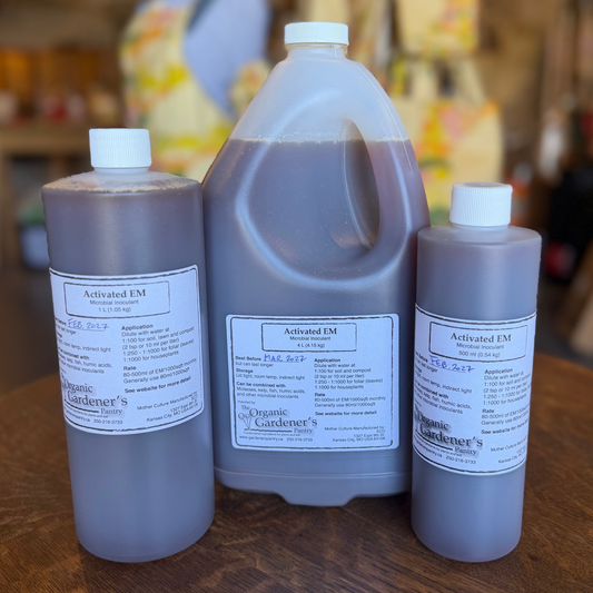 Three plastic bottles of Organic Gardener's Activated EM liquid fertilizer in different sizes arranged on a wooden table, with a blurred shop background.